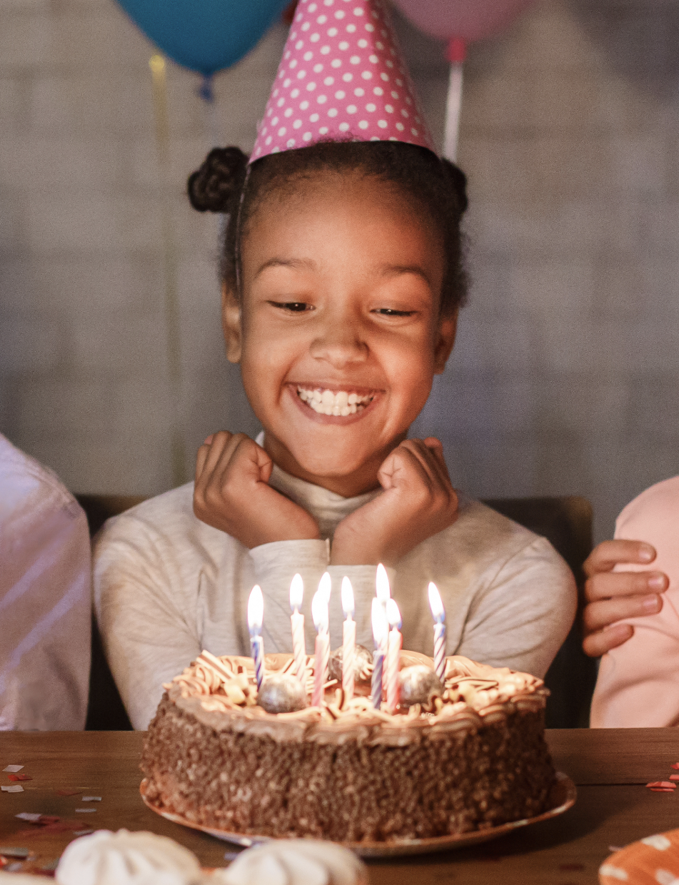 Girl in a party hat smiling at her birthday cake
